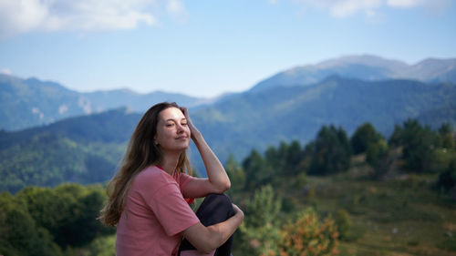 Smiling young woman standing on mountain against sky
