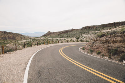 Empty road by mountains against clear sky