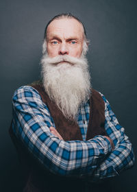 Portrait of confident bearded senior man standing arms crossed over gray background