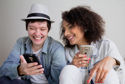 Smiling friends using mobile phone while standing against white background