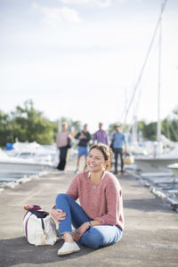 Happy woman sitting on pier with friends standing in background