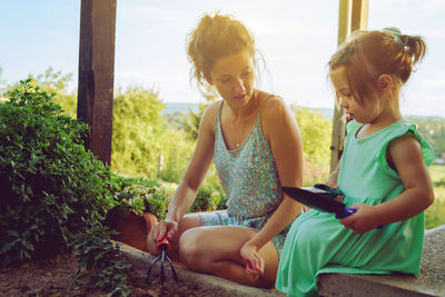 Mother and daughter sitting with equipment by plants