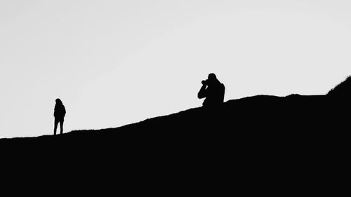 Silhouette people on mountain against clear sky