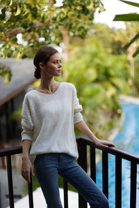 Young woman looking away while standing against trees