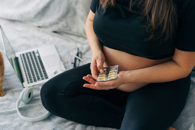 Pregnant unrecognizable woman holds vitamin capsules in her hands.