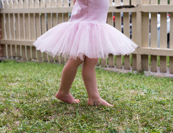 Low section of girl standing on grassy field at yard