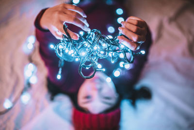 High angle view of woman holding illuminated string light while lying on bed