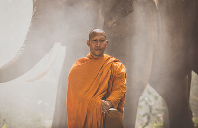 Monk standing by elephant at forest