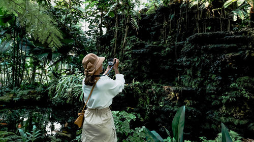 Rear view of woman photographing against trees