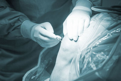 Midsection of doctor performing operation on patient knee in hospital