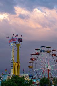 Ferris wheel by illuminated building against sky at sunset