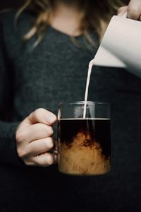 Midsection of woman pouring milk in coffee