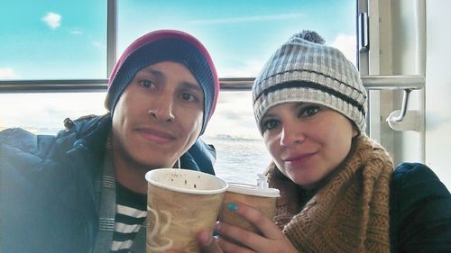 Portrait of friends wearing warm clothing while holding coffee cups against window in ship
