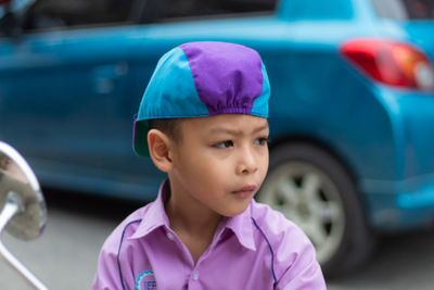 Cute boy looking away while standing against car on road