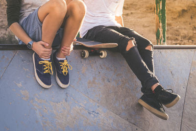 Low section of man and boy sitting in skateboard park