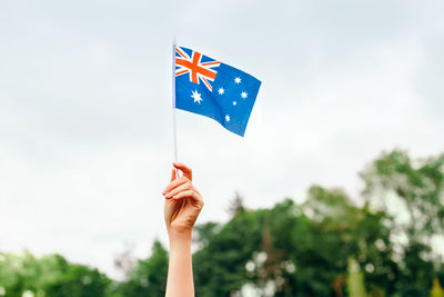 Close-up of hand holding flag against blue sky