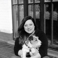 Portrait of smiling woman holding dog while sitting against built structure