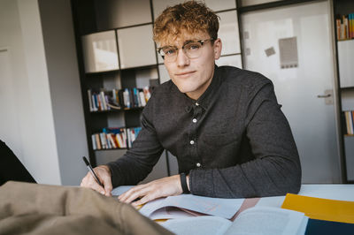 Portrait of confident young blond male student studying in community college