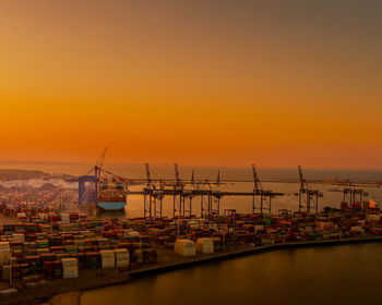 Cranes at harbor against sky during sunset