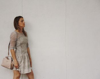 Woman with purse looking away while walking against wall