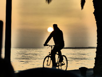 Silhouette man with bicycle on beach against sky during sunset