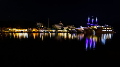 Illuminated cityscape by river against clear sky at night