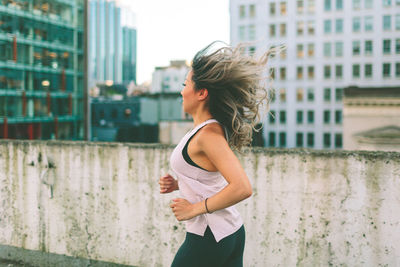 Side view of woman standing against building in city