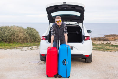 Portrait of man standing by car against sky