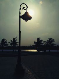 Street light and silhouette palm trees against sky during sunset