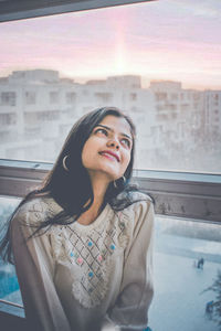 Smiling young woman looking away while sitting by window