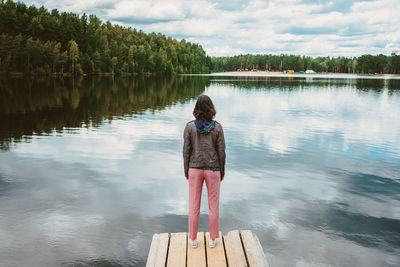 Top view of a lonely girl standing on the pier of a forest lake