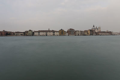 View of buildings by river against cloudy sky