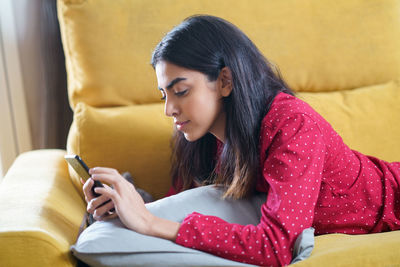 Young woman using mobile phone while lying on sofa