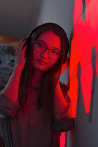 Young smiling woman with headphones in red neon light listening to music, nightclub futuristic neon