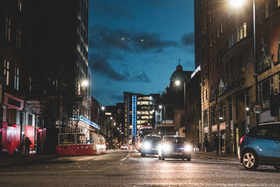 Cars on illuminated road by buildings in city at night