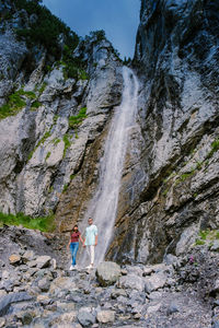 Rear view of woman standing on rock against waterfall