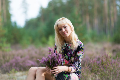 Portrait of young woman with blond hair holding flowers on field