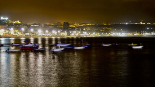 Illuminated city by river against sky at night