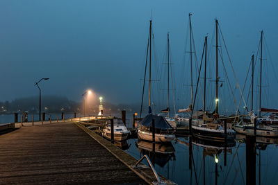 Sailboats moored at harbor against sky during dusk