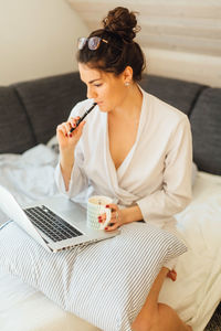 Young woman using phone while sitting on sofa at home