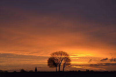 Silhouette trees on field against romantic sky at sunset