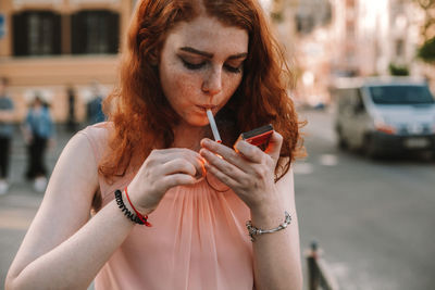 Young woman with freckles lighting cigarette while standing in street