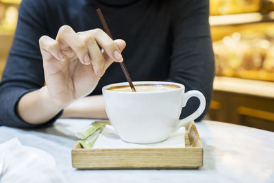 Midsection of woman stirring cappuccino at table