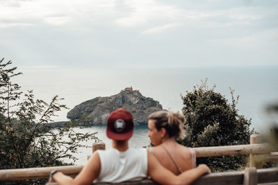 Rear view of couple sitting on bench against sea and sky