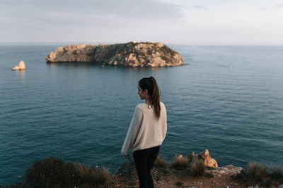 Woman standing on rock looking at sea against sky with island