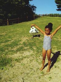 Full length of girl standing with arms outstretched on field during sunny day