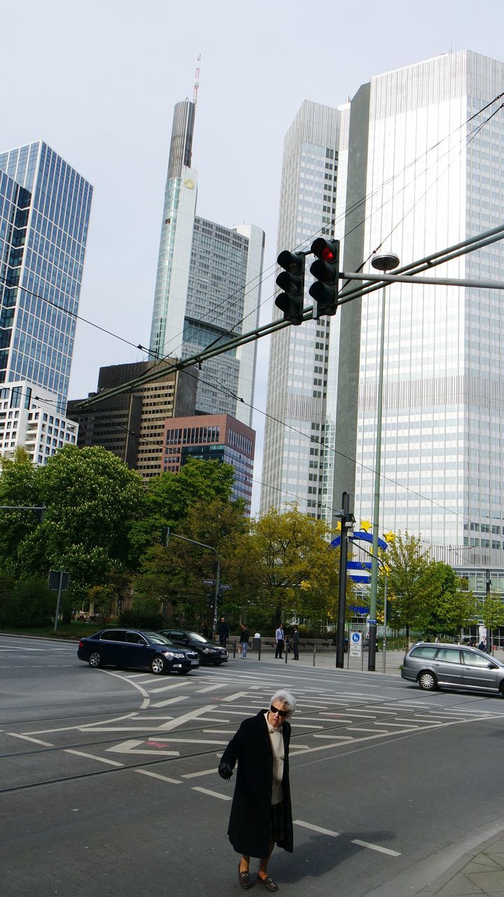 building exterior, architecture, built structure, city, street, men, transportation, city life, road, clear sky, land vehicle, tall - high, car, tower, walking, skyscraper, city street, modern