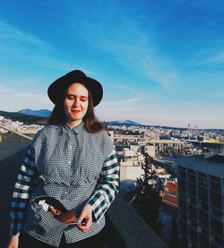 Portrait of smiling young woman standing against cityscape