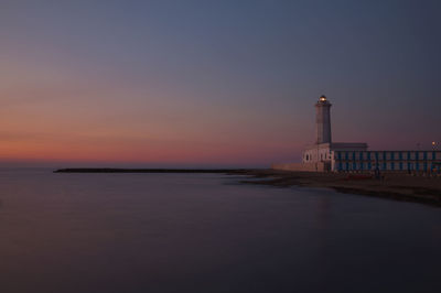 Lighthouse by sea against clear sky during sunset