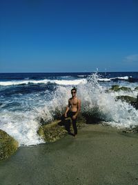 Full length of shirtless man on beach against clear sky